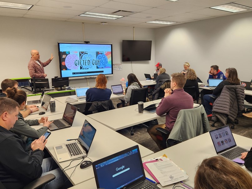 people sitting at tables with laptops and guy presenting