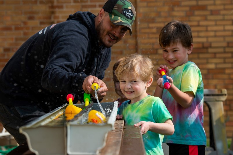 guy standing with 2 boys squirting water