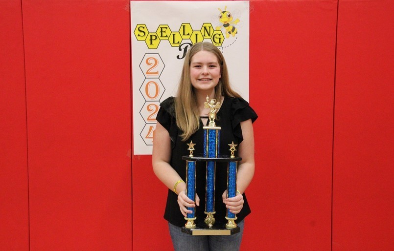 GIRL HOLDING BLUE TROPHY FOR SPELLING BEE